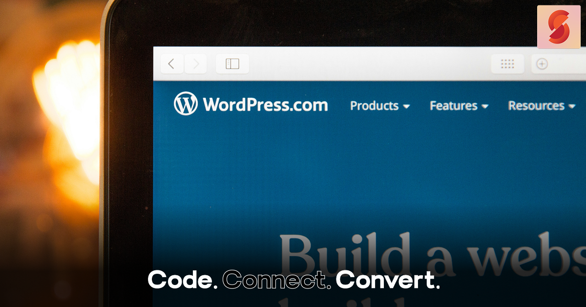 A close-up of a laptop screen displaying the WordPress.com homepage, with its logo and navigation menu visible against a blue background.