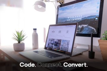 A modern and bright desk setup featuring a laptop displaying a data analytics dashboard, a large monitor with a "Work Hard Anywhere" wallpaper, and several potted plants.