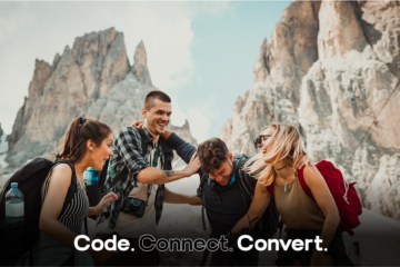 A group of four happy friends laugh together while hiking in a dramatic mountain setting, with a cable car visible in the background.