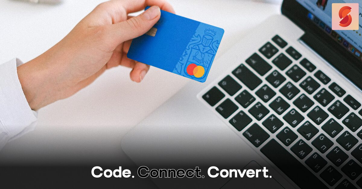 A close-up of a person's hand holding a blue credit card above a laptop keyboard, preparing to make an online payment.