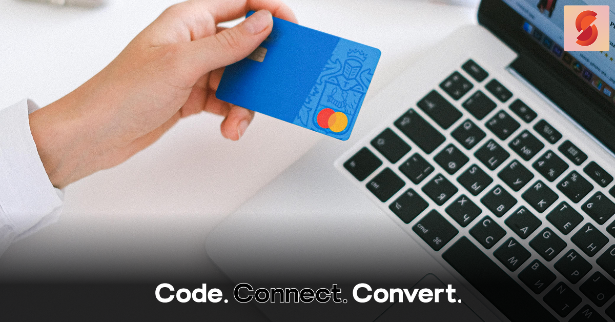 A close-up of a person's hand holding a blue credit card above a laptop keyboard, preparing to make an online payment.