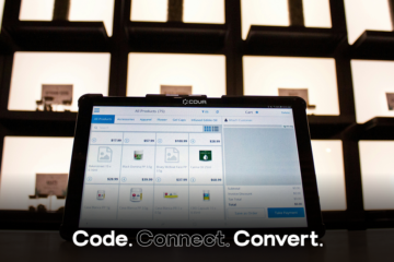 A tablet-based point-of-sale system on a counter displays a digital product catalog inside a modern retail store with backlit display shelves.