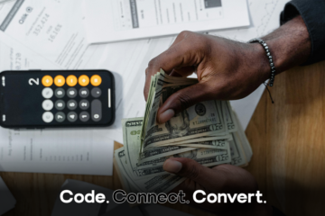 An overhead view of a person's hands counting a fan of US dollar bills over a desk scattered with financial documents and a smartphone showing a calculator.